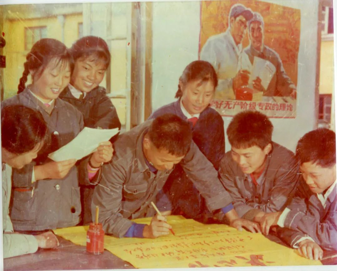 A group of people writing on a large yellow paper

Description automatically generated