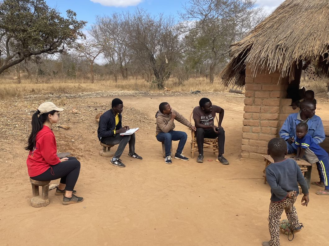 A group of people sitting outside a hut

Description automatically generated